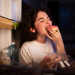 A woman is eating a donut in the kitchen